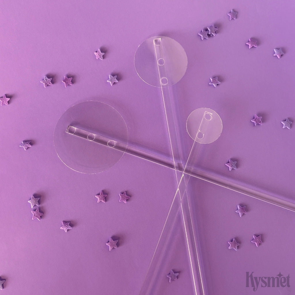 Three clear plastic sticks with clear circles on the ends are surrounded by star sprinkles against a purple background.