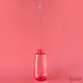 A pink bottle holds a clear plastic stick with a clear clothespin at the top, against a pink background.