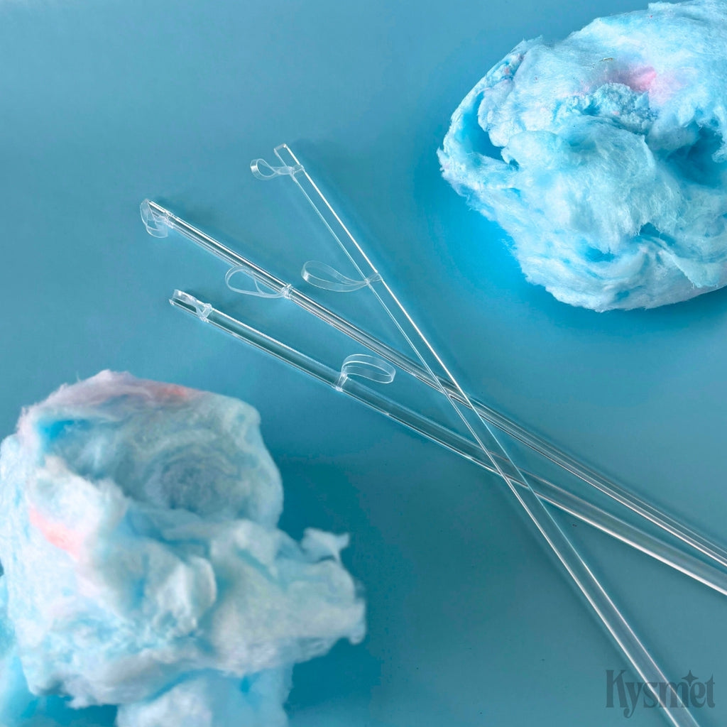 Three clear sticks with clear rubberbands attached are surrounded by blue cotton candy against a blue background.