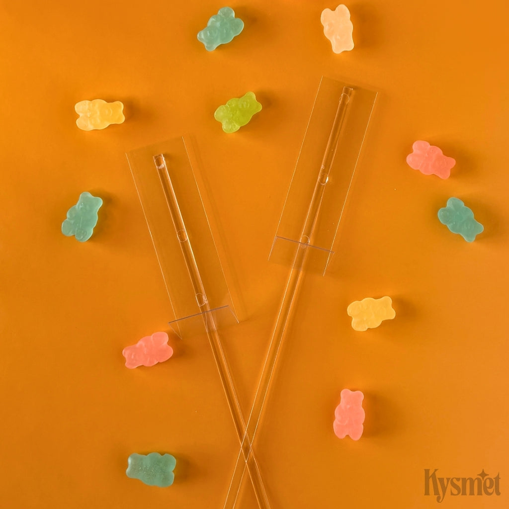 Two plastic sticks with clear rectangles are surrounded by gummy bears against an orange background.