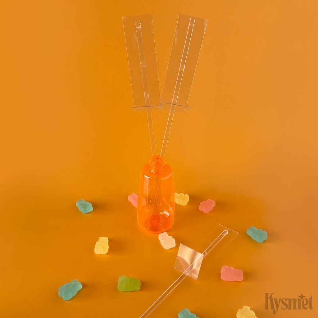 Three clear plastic sticks with clear rectangles attached, an orange plastic bottle, gummy bears, set against an orange background.