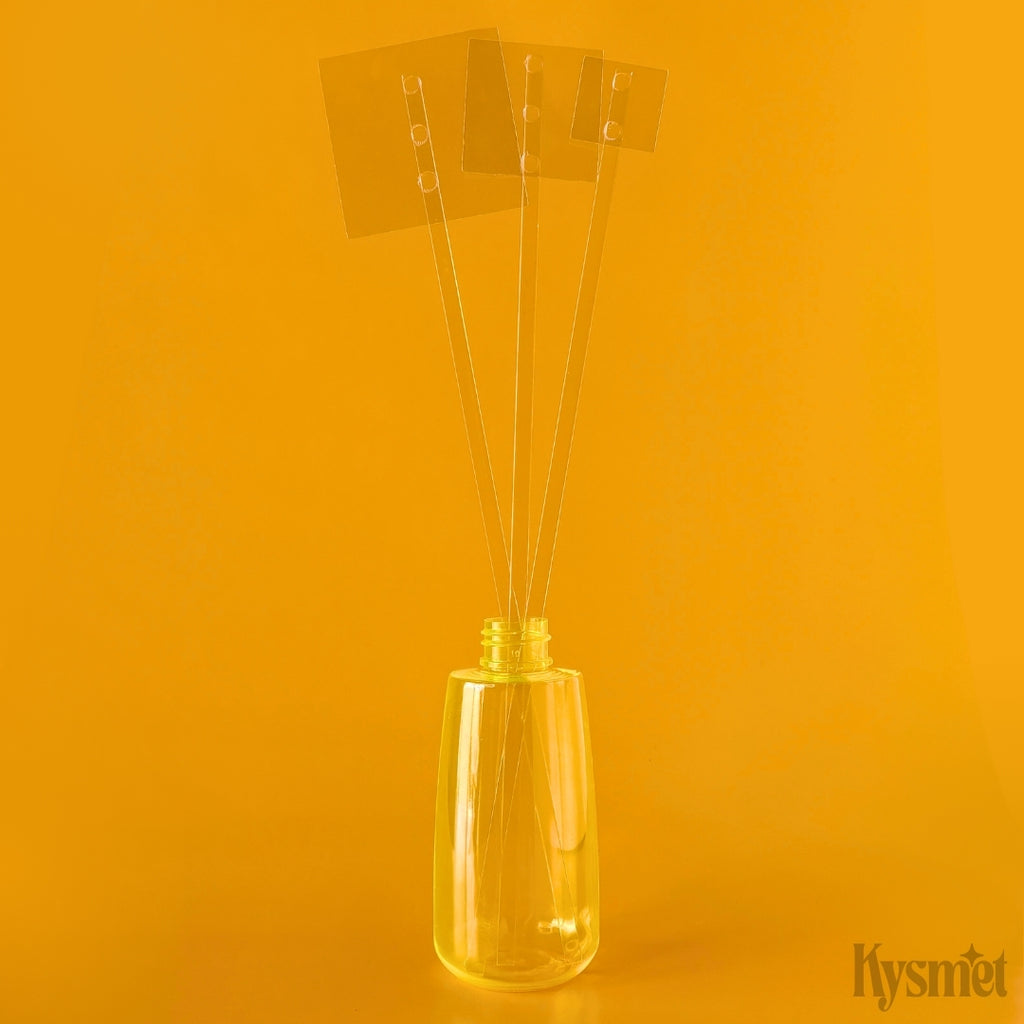 An orange plastic bottle holds three clear plastic sticks each with a square piece of acetate at the top, against an orange background.
