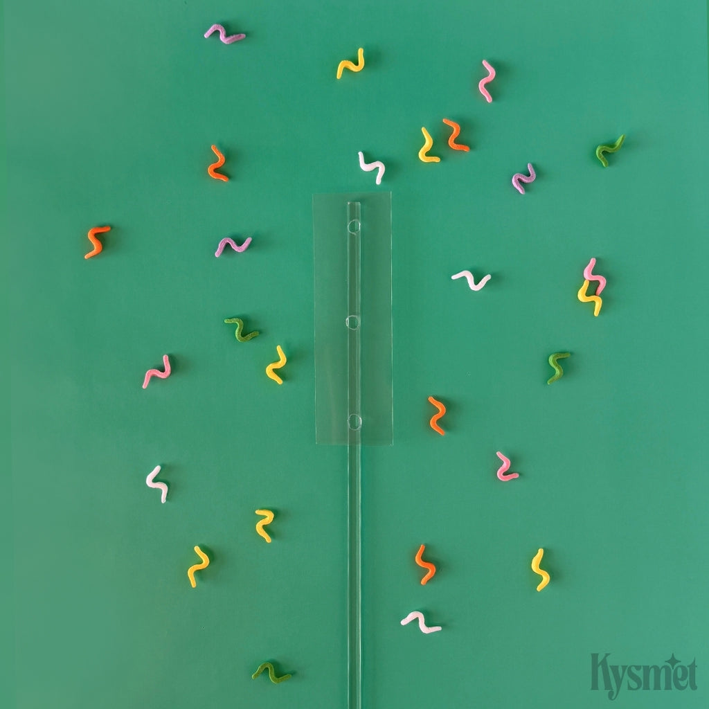 A clear plastic stick with a clear rectangle attached is surrounded by colorful swiggles against a green background.